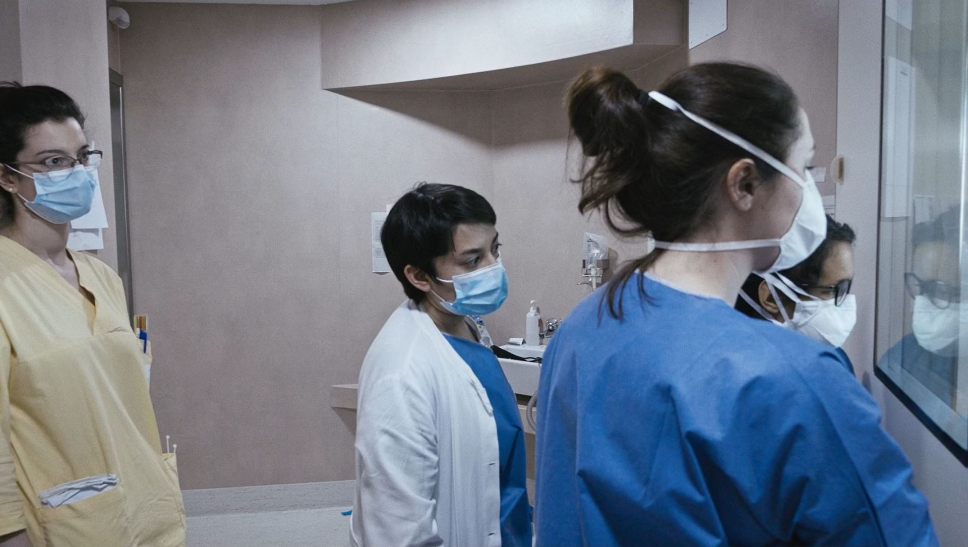 Il personale degli Infettivi assiste con preoccupazione a un delicato intervento dall'esterno di una stanza in cui è ricoverata una paziente che si sta aggravando